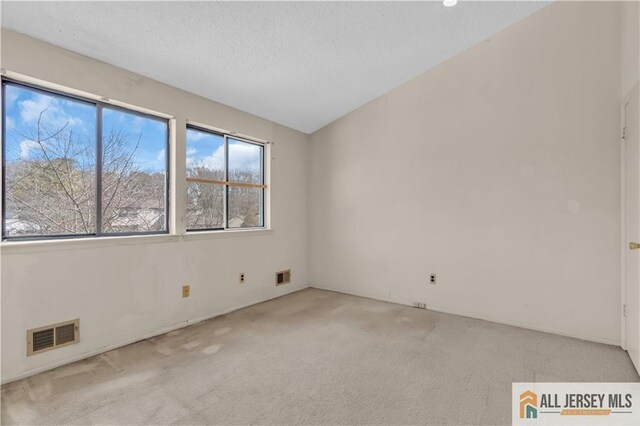 empty room featuring a textured ceiling, lofted ceiling, visible vents, and light carpet