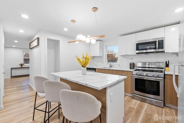 kitchen featuring sink, a center island, hanging light fixtures, appliances with stainless steel finishes, and white cabinets