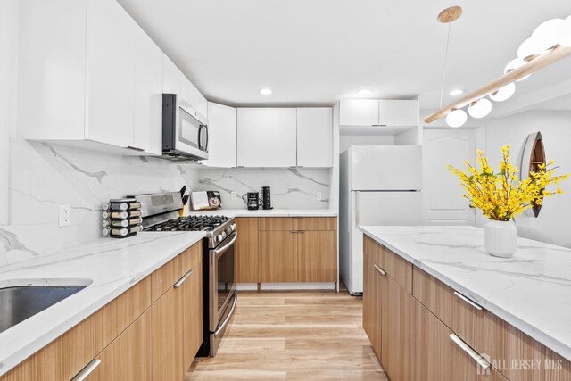 kitchen with light stone counters, appliances with stainless steel finishes, light hardwood / wood-style flooring, and white cabinets