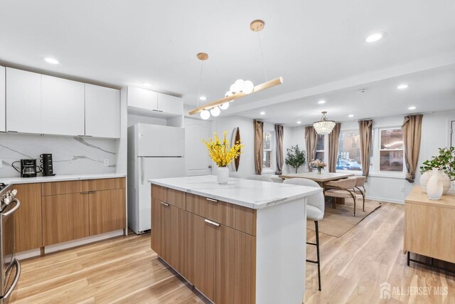 kitchen with white cabinetry, decorative light fixtures, light hardwood / wood-style flooring, white refrigerator, and a kitchen island