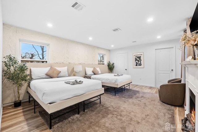 bedroom with light wood finished floors, a fireplace with flush hearth, visible vents, and recessed lighting