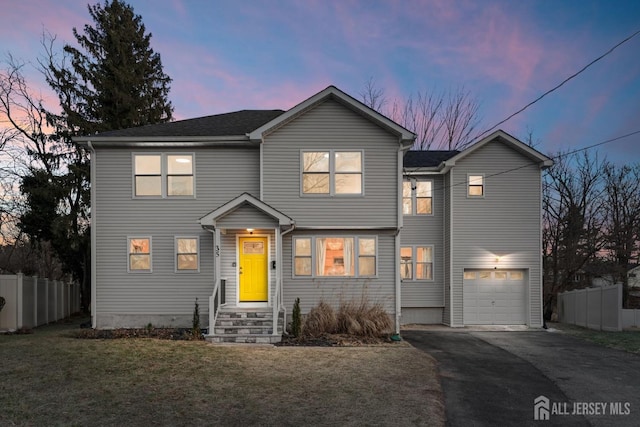 traditional-style house featuring a front lawn, fence, driveway, and an attached garage