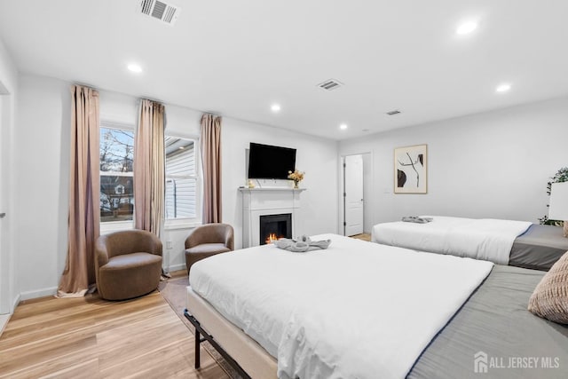 bedroom with recessed lighting, visible vents, a lit fireplace, and light wood finished floors