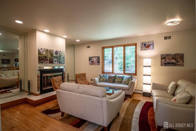 living room with wood finished floors, a baseboard heating unit, recessed lighting, a glass covered fireplace, and baseboards