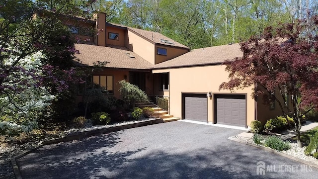 view of front facade featuring an attached garage, asphalt driveway, stucco siding, and roof with shingles