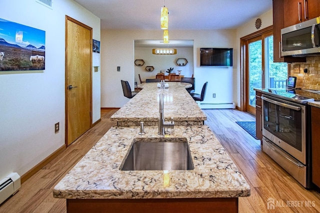kitchen featuring appliances with stainless steel finishes, a kitchen island with sink, a baseboard radiator, and a sink