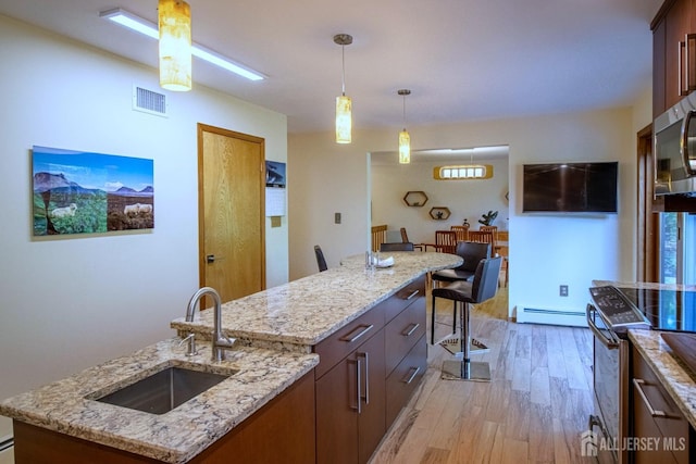 kitchen featuring a sink, appliances with stainless steel finishes, light wood finished floors, a baseboard heating unit, and pendant lighting