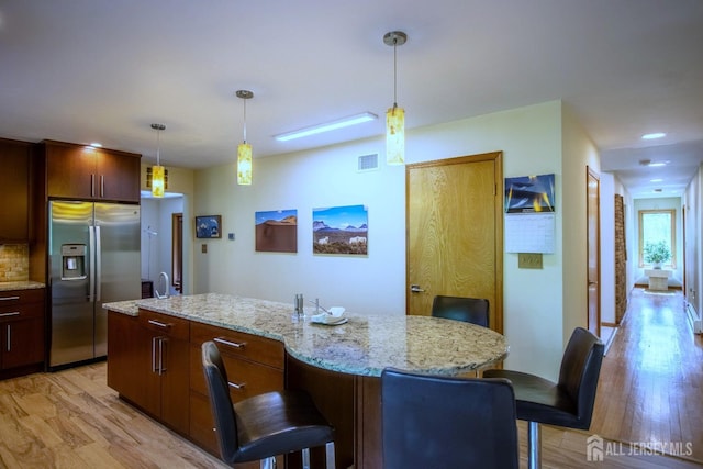 kitchen featuring stainless steel fridge, light wood-style flooring, a center island, a kitchen breakfast bar, and decorative light fixtures