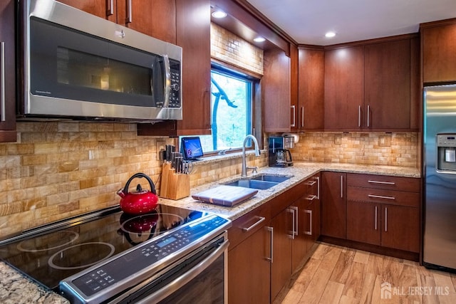 kitchen featuring stainless steel appliances, a sink, light wood-type flooring, light stone countertops, and tasteful backsplash