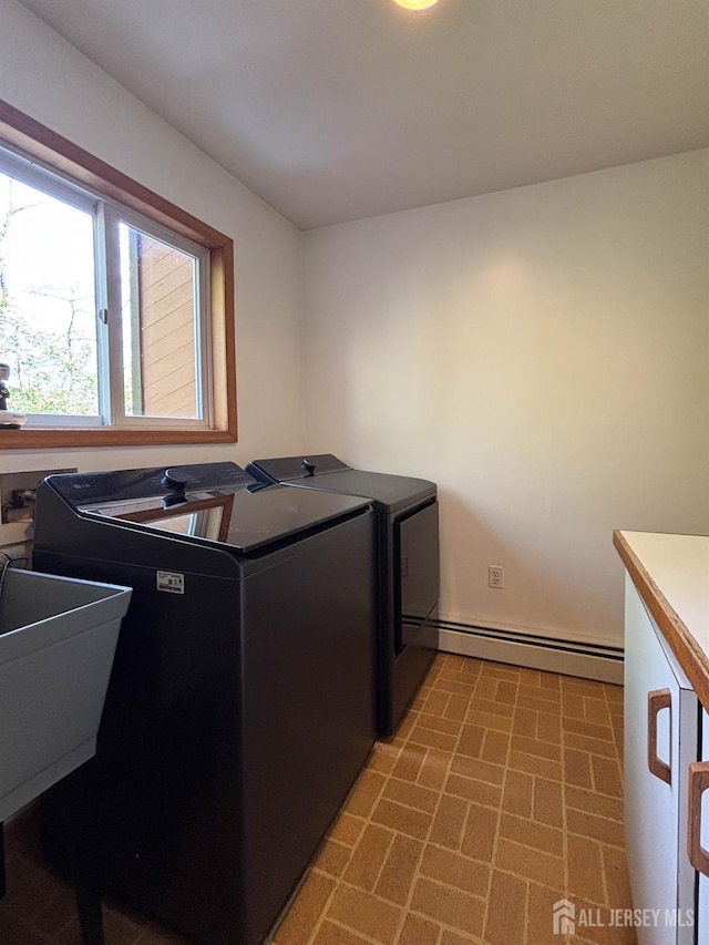 clothes washing area with washing machine and dryer, baseboard heating, brick patterned floors, and baseboards