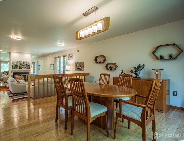 dining room featuring a glass covered fireplace, light wood-type flooring, and baseboards