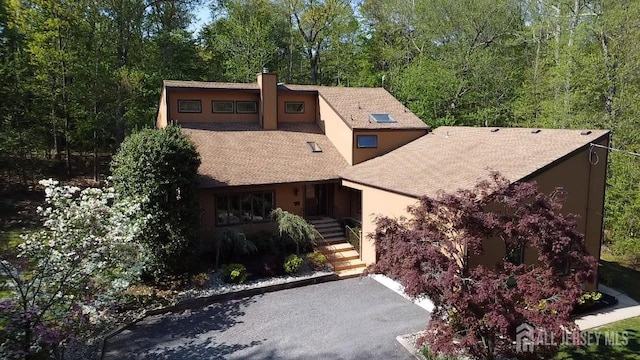 view of front of property featuring stucco siding, a chimney, and roof with shingles