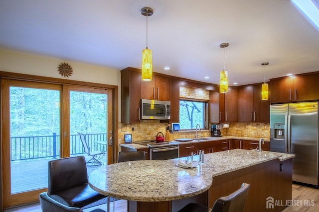 kitchen with stainless steel appliances, a kitchen breakfast bar, decorative backsplash, light stone countertops, and an island with sink
