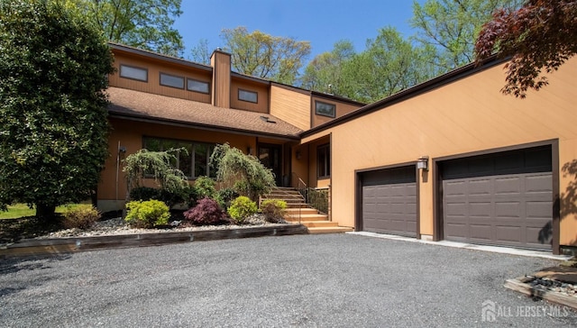 view of front of home with an attached garage, asphalt driveway, a chimney, and stucco siding