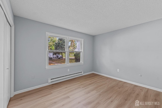 unfurnished bedroom featuring a baseboard heating unit, a textured ceiling, a closet, and light wood-style flooring