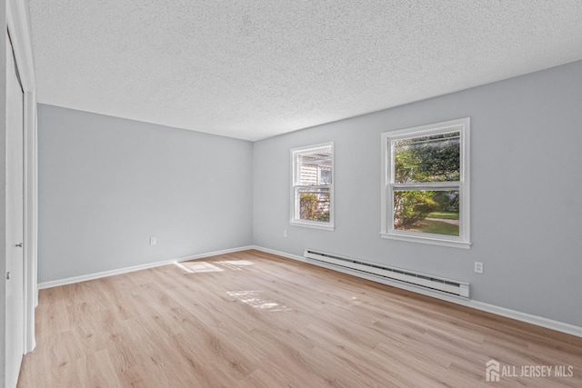 unfurnished room featuring a textured ceiling, a baseboard heating unit, baseboards, and wood finished floors