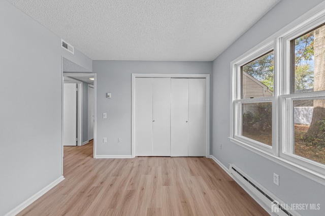 unfurnished bedroom with baseboards, baseboard heating, light wood-style flooring, a closet, and a textured ceiling