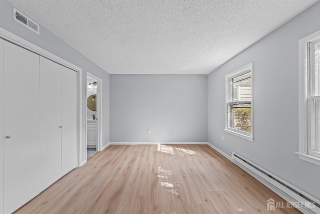 interior space with visible vents, baseboards, baseboard heating, light wood-style floors, and a textured ceiling