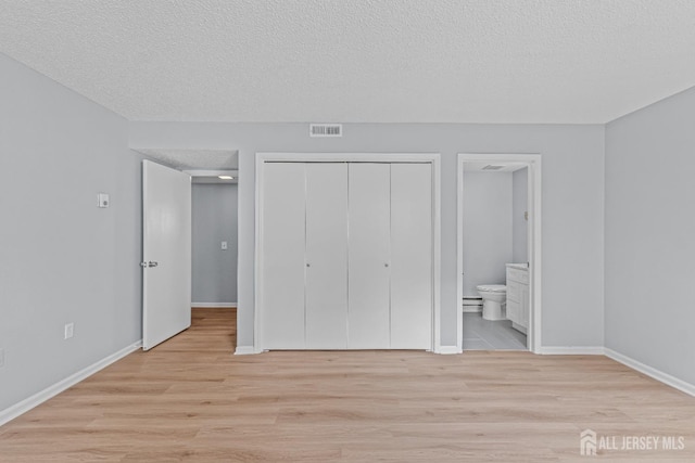 unfurnished bedroom with ensuite bath, light wood-style floors, visible vents, and a closet