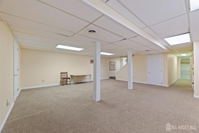 finished below grade area with light carpet, a paneled ceiling, visible vents, and baseboards