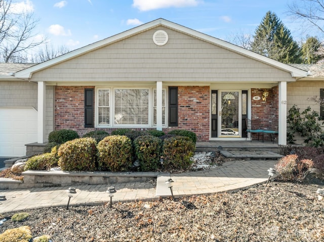 single story home featuring a porch, a garage, and brick siding