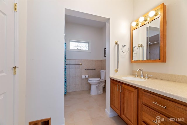 bathroom featuring tile walls, visible vents, toilet, vanity, and tile patterned flooring