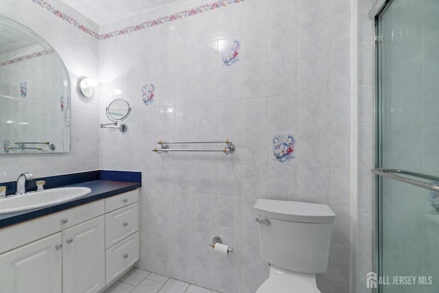 bathroom featuring toilet, a shower with shower door, vanity, tile walls, and tile patterned floors