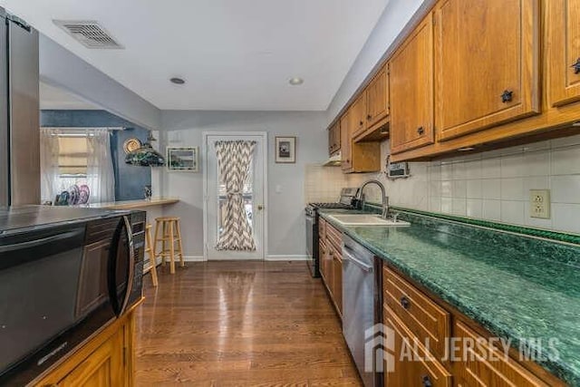 kitchen featuring brown cabinetry, visible vents, decorative backsplash, appliances with stainless steel finishes, and dark countertops