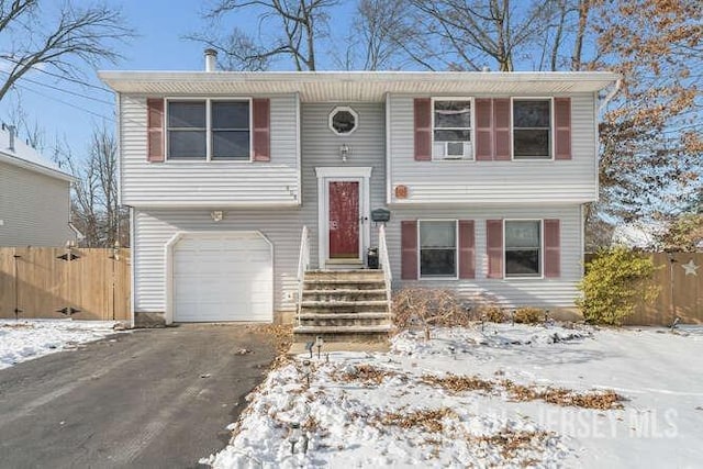 bi-level home featuring cooling unit, an attached garage, driveway, and fence