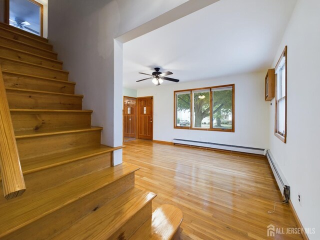 stairway with baseboard heating, ceiling fan, and wood-type flooring