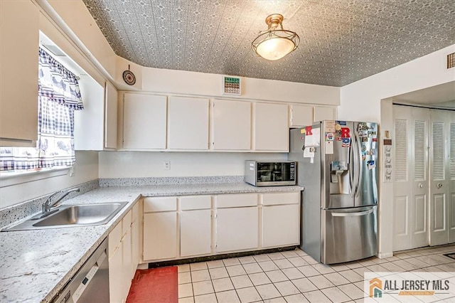 kitchen featuring appliances with stainless steel finishes, sink, light tile patterned floors, and white cabinets