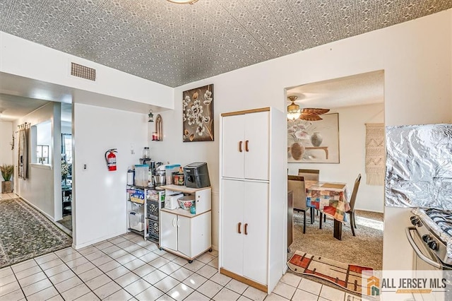 kitchen with white cabinetry, light colored carpet, stainless steel stove, and ceiling fan