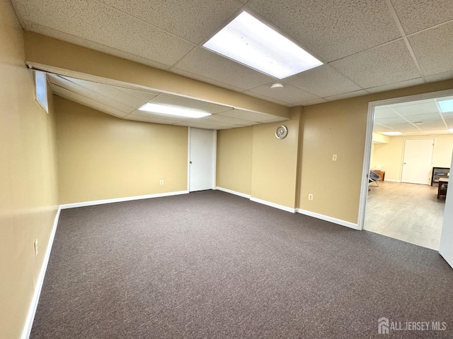 finished basement with baseboards, a paneled ceiling, and dark colored carpet