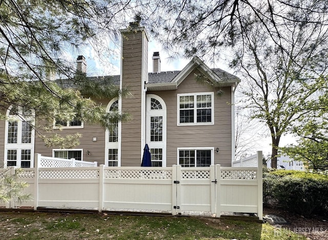 rear view of property featuring fence, a gate, and a chimney