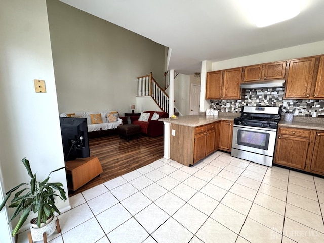 kitchen with brown cabinetry, a peninsula, gas range, under cabinet range hood, and light tile patterned floors