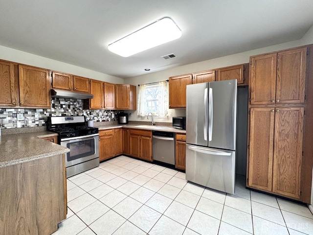 kitchen featuring visible vents, brown cabinetry, under cabinet range hood, a sink, and appliances with stainless steel finishes