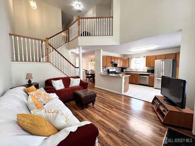 living area featuring light wood-style flooring, stairway, and a towering ceiling