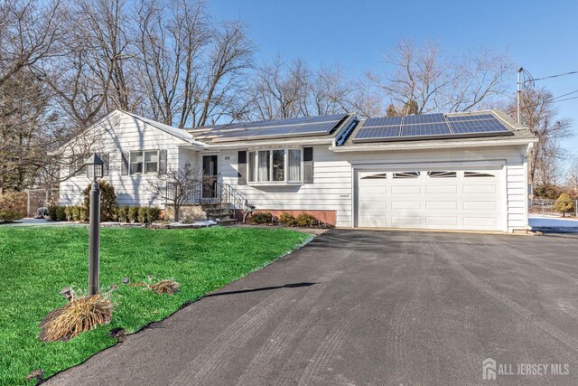 ranch-style home featuring a garage, a front yard, and solar panels