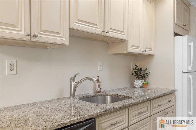 kitchen with freestanding refrigerator, cream cabinetry, light stone counters, and a sink