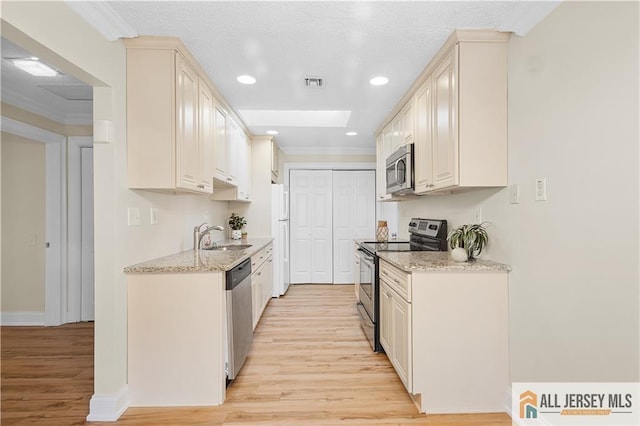 kitchen with visible vents, appliances with stainless steel finishes, a sink, ornamental molding, and light wood-style flooring