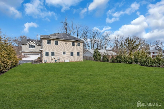 back of property featuring an attached garage, a yard, and fence