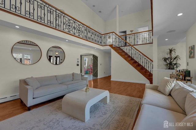 living area featuring wood finished floors, recessed lighting, arched walkways, stairs, and a towering ceiling