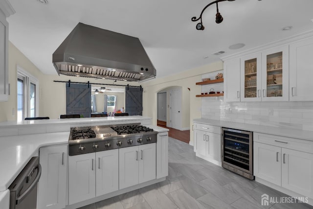 kitchen with wine cooler, a barn door, exhaust hood, arched walkways, and stainless steel appliances