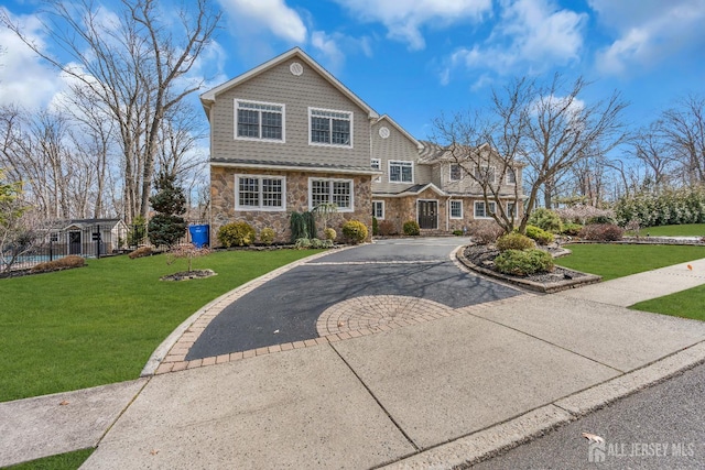 shingle-style home featuring a front yard, fence, stone siding, and driveway