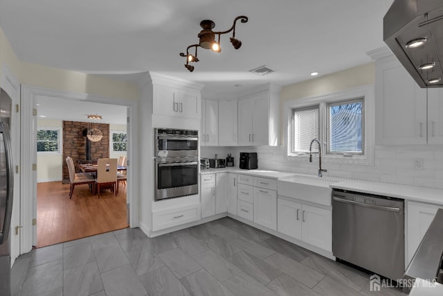 kitchen featuring a sink, tasteful backsplash, white cabinetry, appliances with stainless steel finishes, and wall chimney exhaust hood