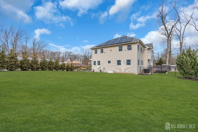 rear view of house with solar panels, a yard, central AC unit, and fence