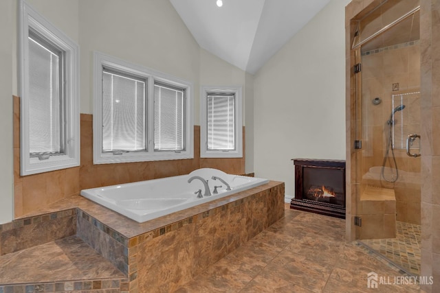 full bath with a bath, a glass covered fireplace, a shower stall, and lofted ceiling