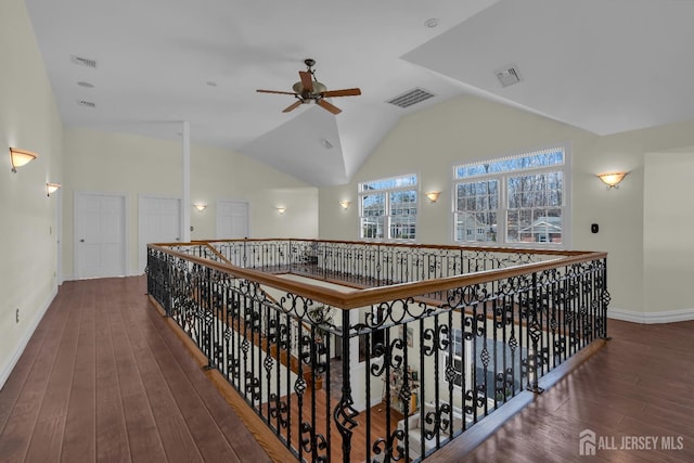 corridor with visible vents, baseboards, hardwood / wood-style floors, and vaulted ceiling