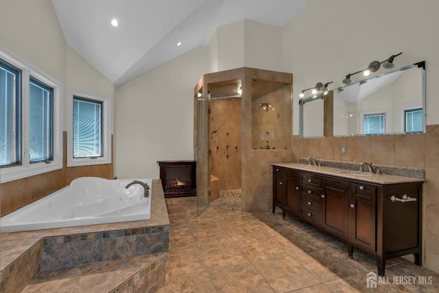 bathroom featuring double vanity, vaulted ceiling, a shower stall, a glass covered fireplace, and a garden tub