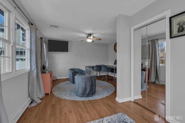 living area with visible vents, baseboards, wood finished floors, and a ceiling fan